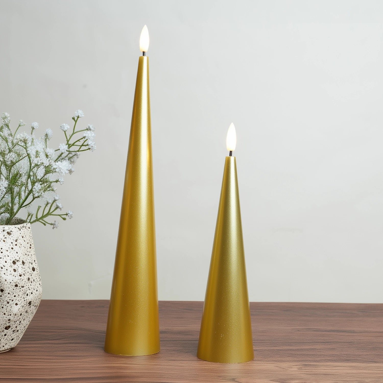 Two gold cone-shaped candles on a wooden surface with a neutral background