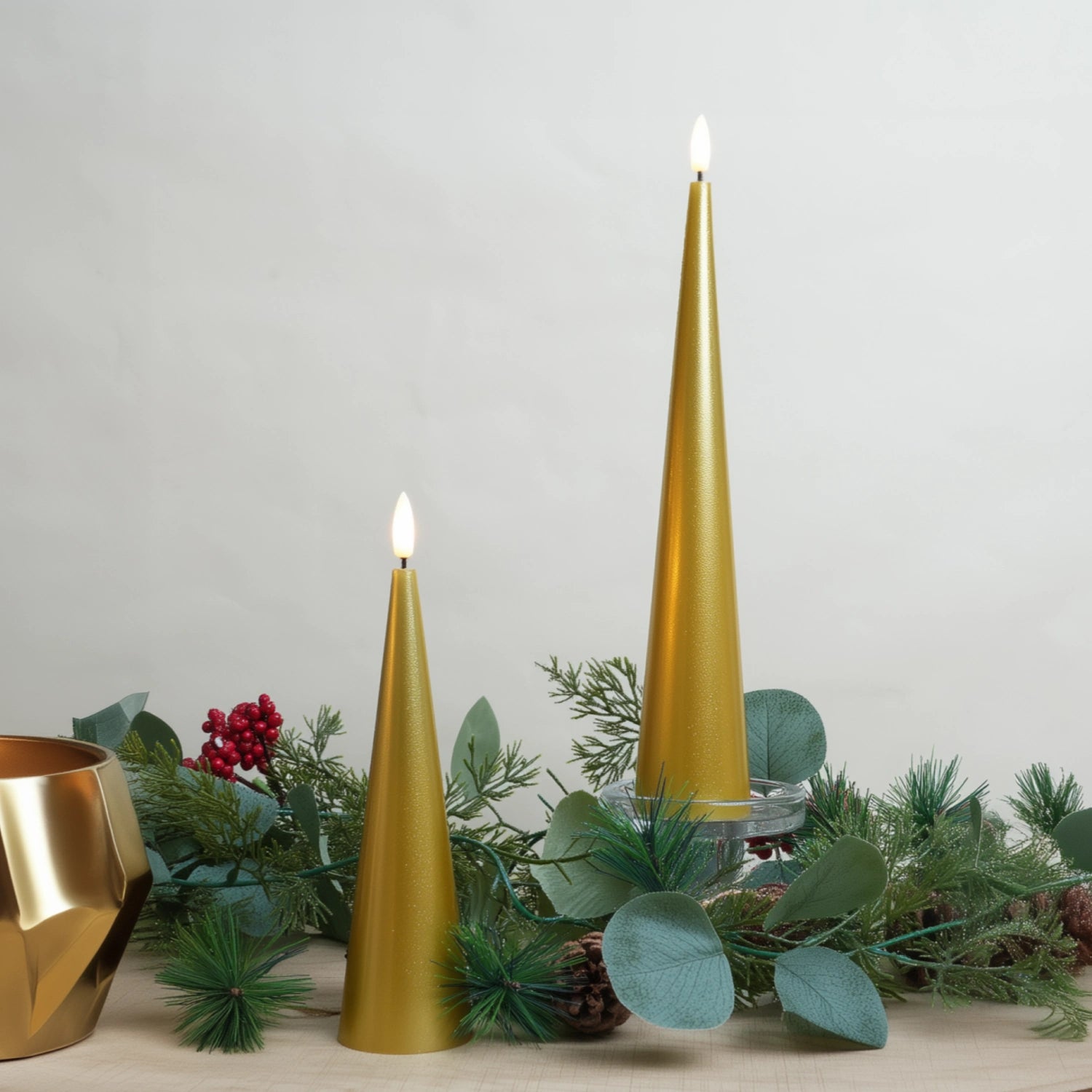 Gold taper candles with greenery on a neutral background