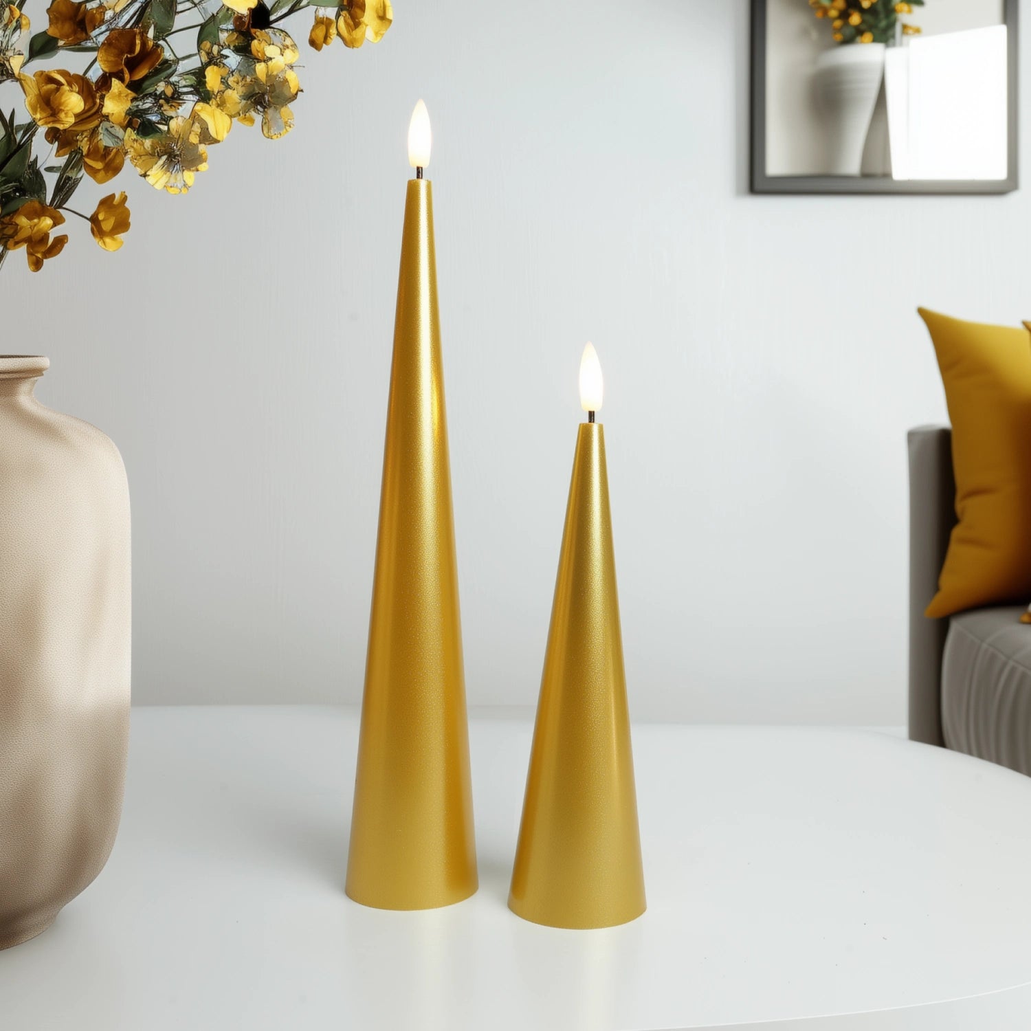 Two gold candles on a white surface with a vase and mirror in the background.