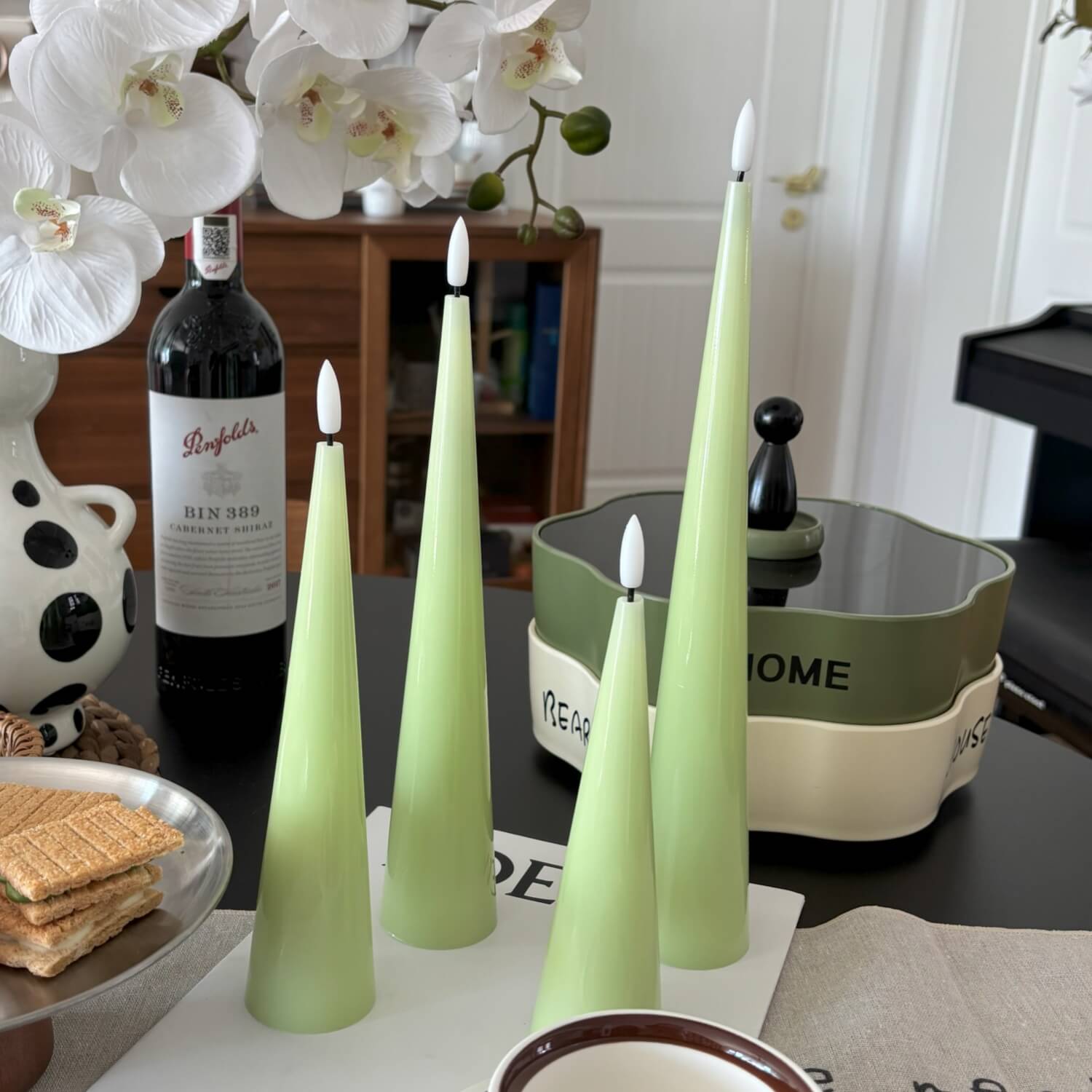 Green candles on a table with a bottle of wine and decorative items.