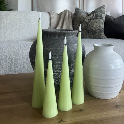 Green candles and a white vase on a wooden table with a sofa in the background