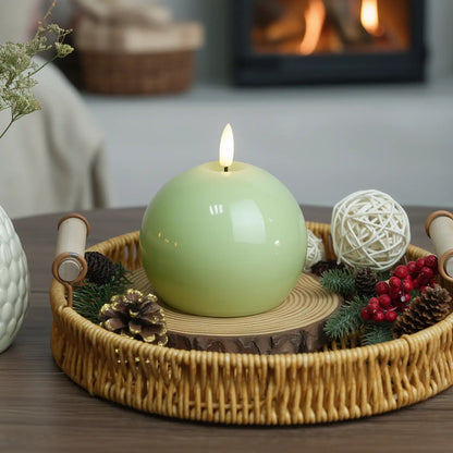 Green spherical candle with a wooden coaster on a table with Christmas decorations.