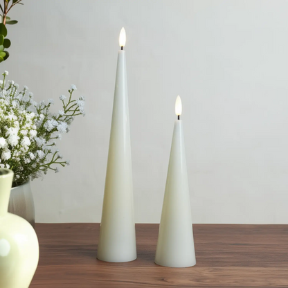 Two cone-shaped candles with greenery on a wooden surface