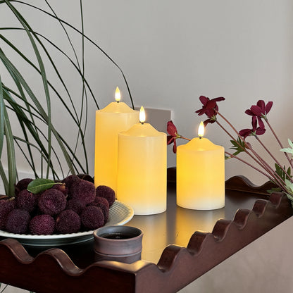 Three lit candles on a decorative stand with purple fruits and flowers.