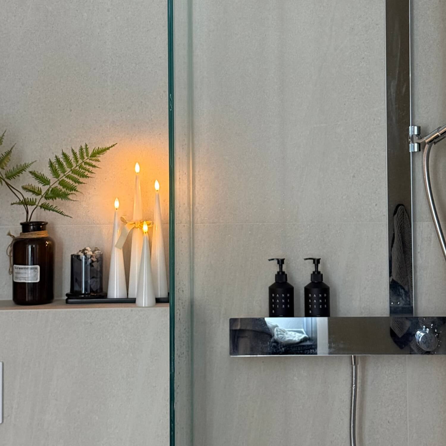 Bathroom setting with candles, bottles, and a plant reflected in a mirror.
