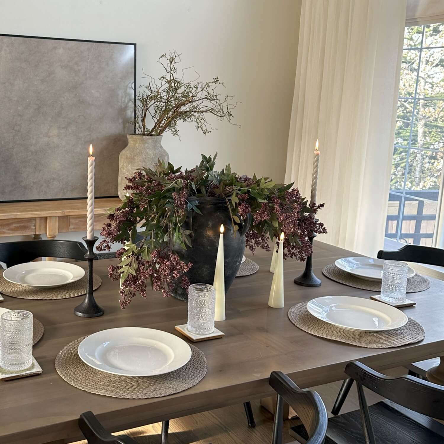 Dining table set with plates, candles, and flowers in a well-lit room.