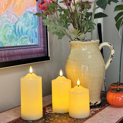Three lit candles on a table with a decorative vase and flowers in the background.