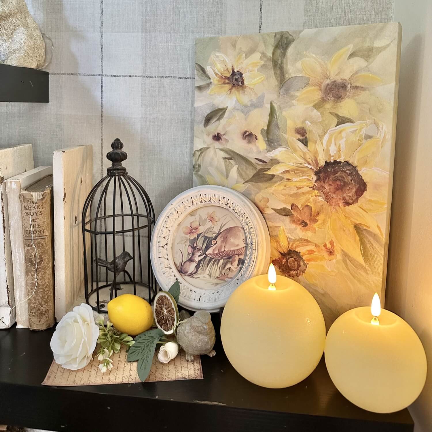 Decorative setup with candles, a painting of sunflowers, and a birdcage on a shelf.