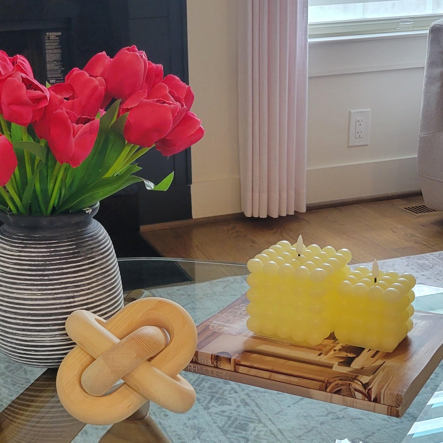 Yellow candle sculptures on a wooden stand with a vase of red tulips in the background.