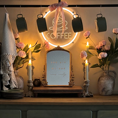 Decorative setup with a mirror, candles, flowers, and a 'Coffee' sign in a warm setting.