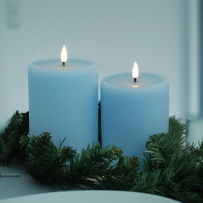 Two blue candles with greenery on a light background