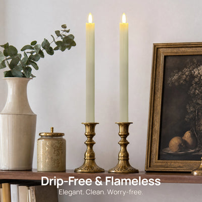 Two flameless LED taper candles in brass candlesticks displayed on a shelf next to a vase with eucalyptus, a small jar, and a framed painting. Text overlay at the bottom reads 'Drip-Free & Flameless Elegant.
