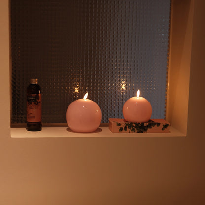 Two pink candles on a shelf with a bottle in front of a textured wall.