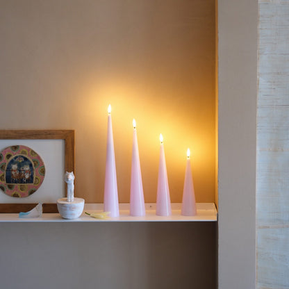 Three lit candles on a shelf with a warm glow against a neutral wall.