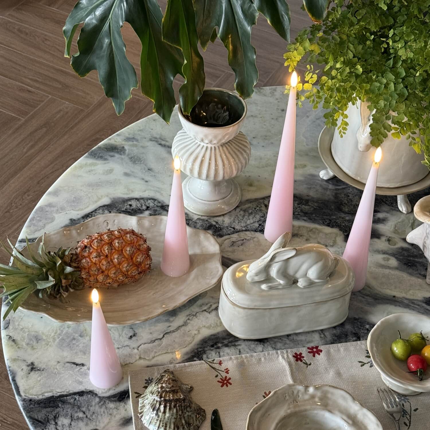 Decorative table setting with pink candles, shells, and plants on a marble surface.