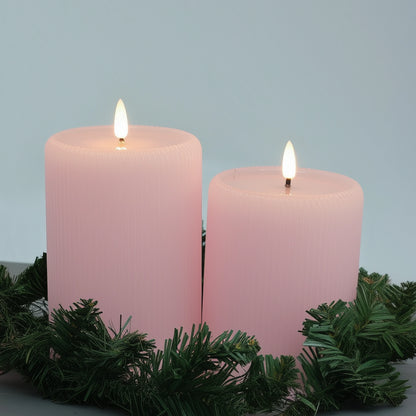 Two pink candles with greenery on a light blue background