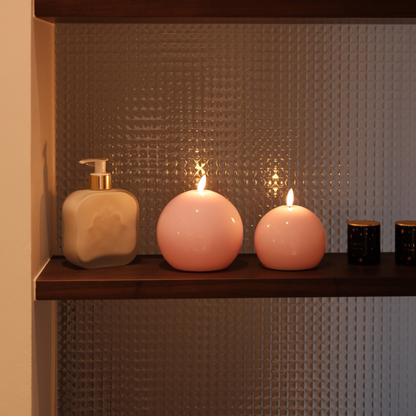 Three candles and a bottle on a shelf against a textured wall.