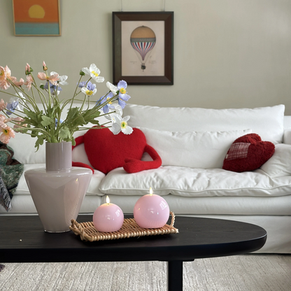 Living room with a white sofa, red heart-shaped pillows, a vase of flowers, and pink candles on a coffee table.