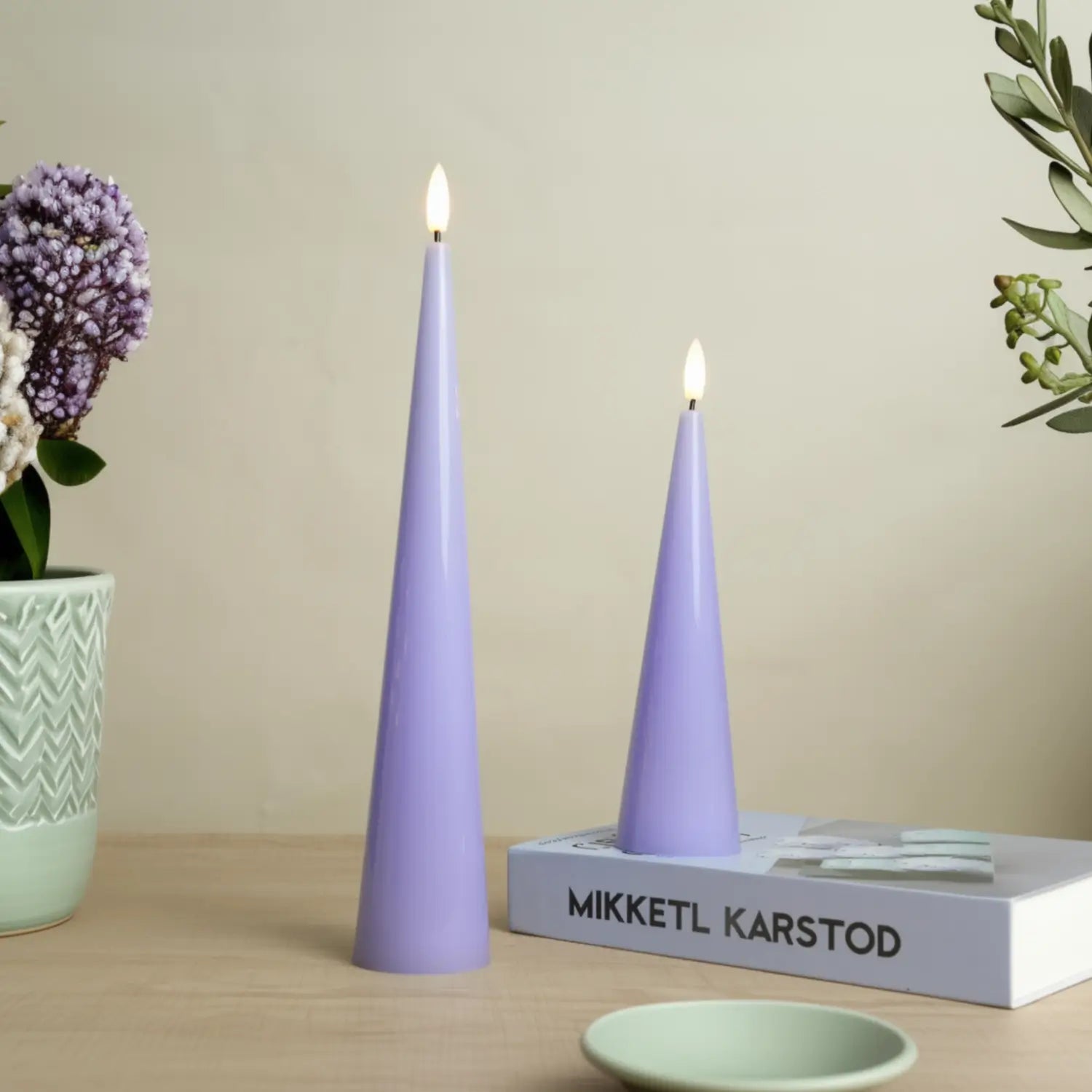 Two purple cone-shaped candles on a wooden surface with a book and decorative items.