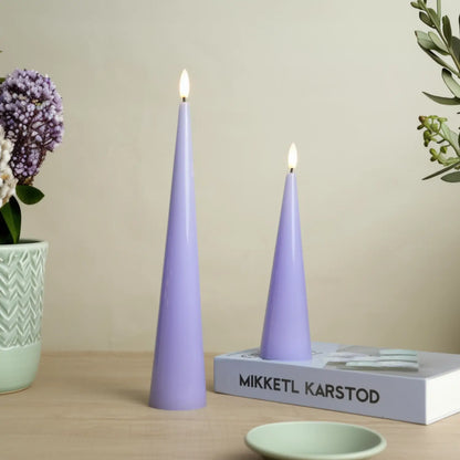 Two purple cone-shaped candles on a wooden surface with a book and decorative items.