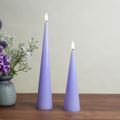 Two purple candles on a wooden surface with a vase of flowers in the background.