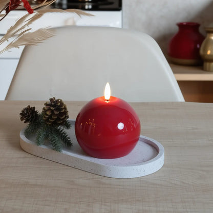 Red spherical candle on a white tray with decorative elements on a wooden surface.
