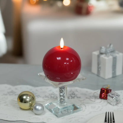 Red spherical candle on a wooden base with a Christmas tree and gift in the background