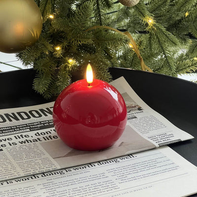 Red spherical candle on a wooden base with a Christmas tree and gift in the background