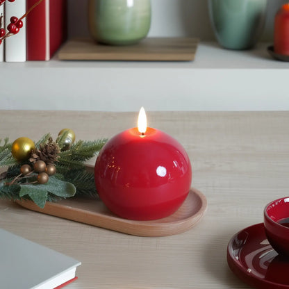 Red candle on a wooden tray with Christmas decorations on a table.