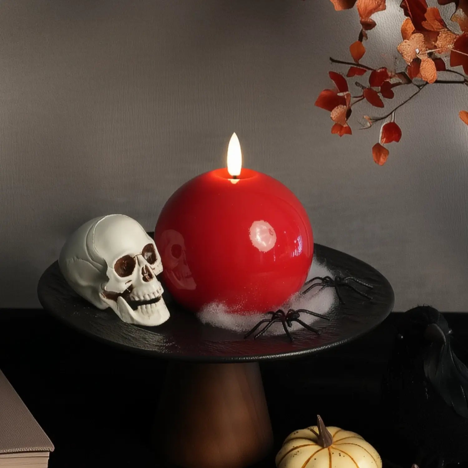 Red candle with a skull and spider on a dark surface against a gray background#color_shiny-red