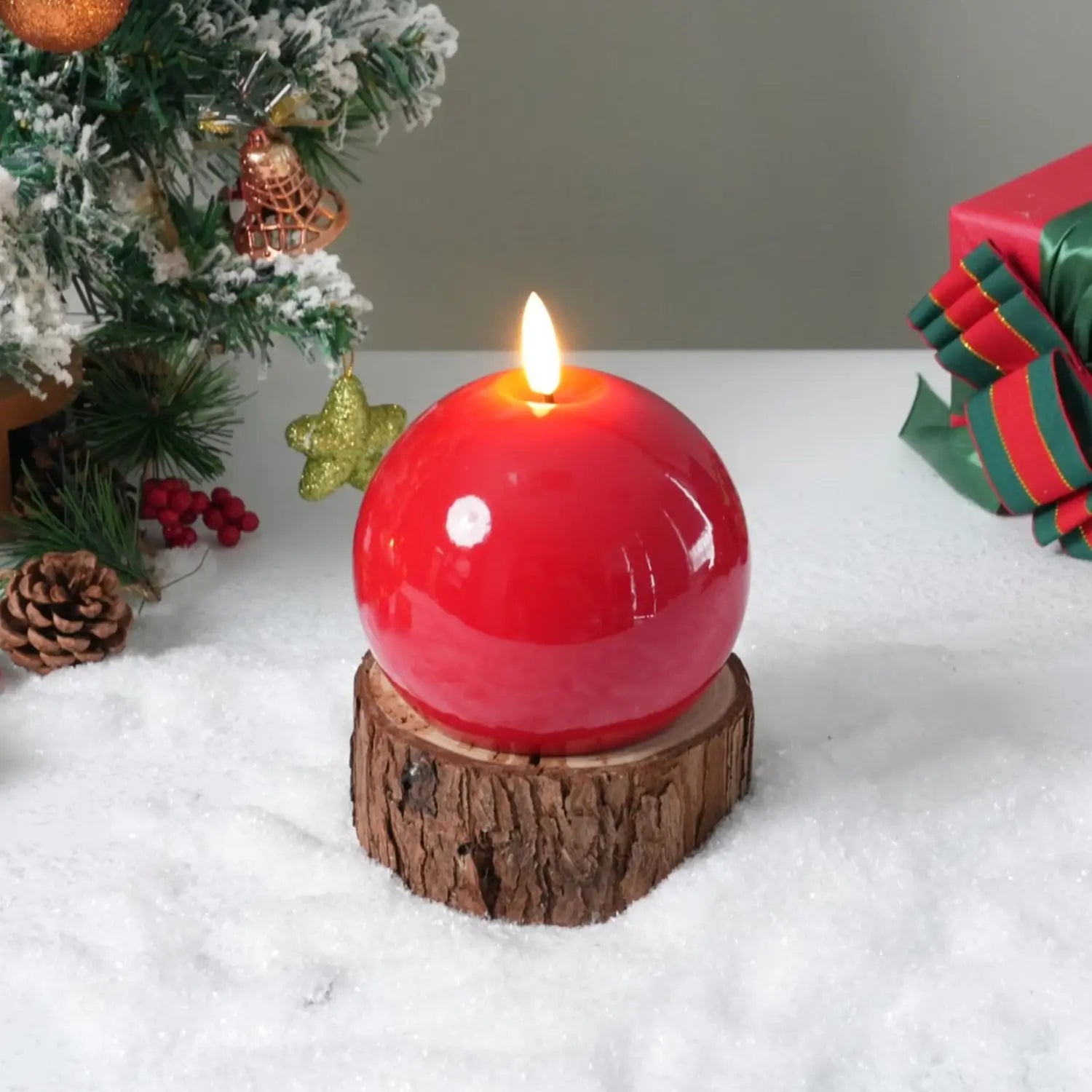 Red spherical candle on a wooden base with a Christmas tree and gift in the background