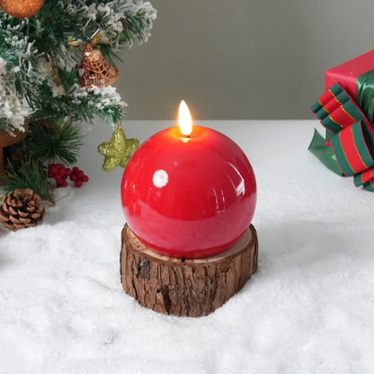 Red spherical candle on a wooden base with a Christmas tree and gift in the background