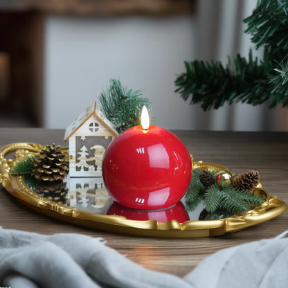 Red candle on a wooden tray with Christmas decorations on a table.