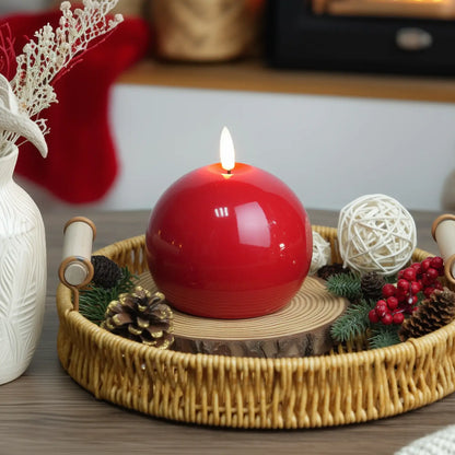 Red candle on a wooden tray with Christmas decorations on a table.