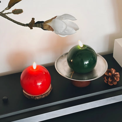 Red candle on a wooden tray with Christmas decorations on a table.