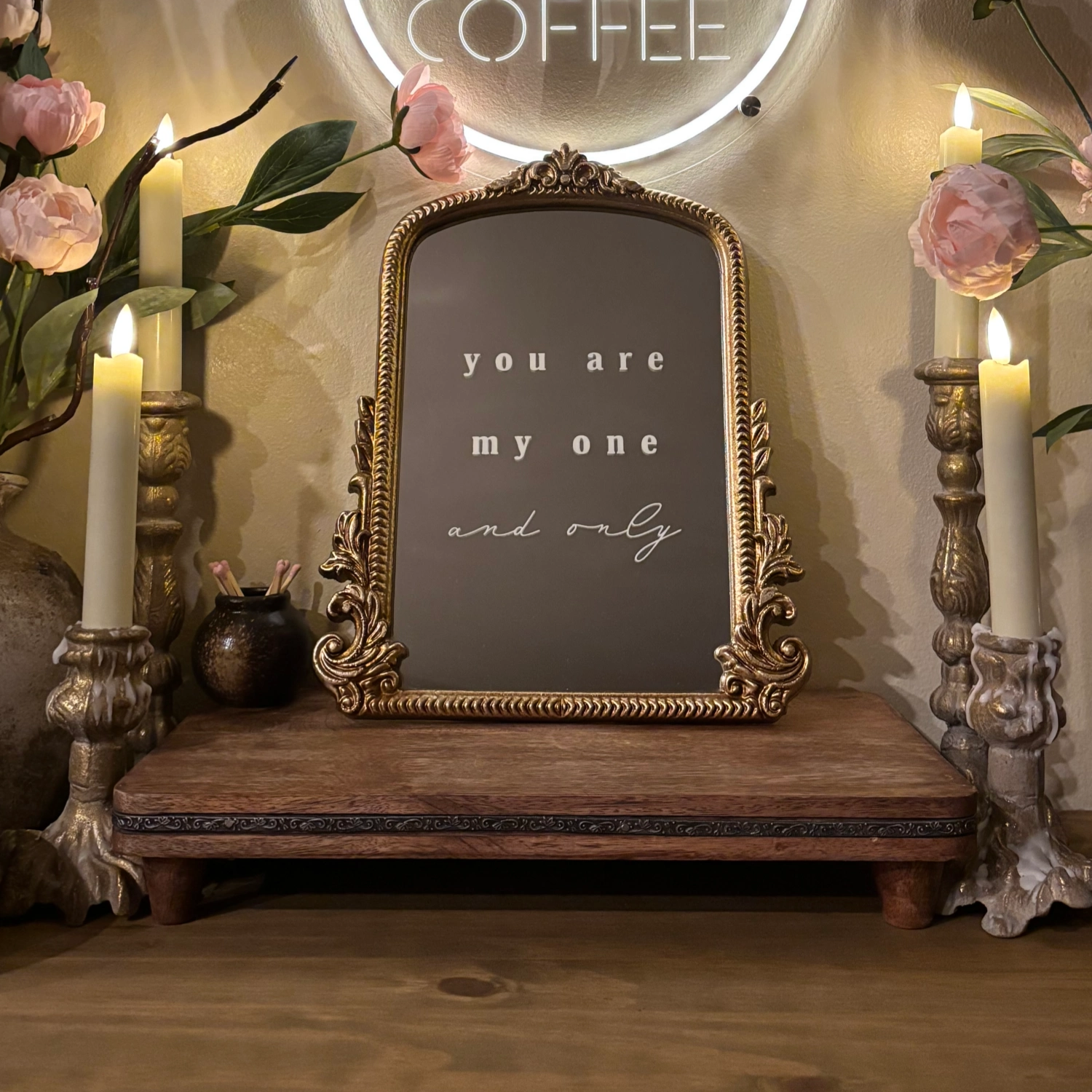 Decorative setup with a framed quote, candles, and flowers on a wooden surface.