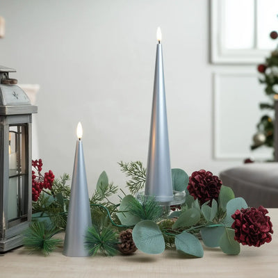 Decorative setup with silver candles, greenery, and red flowers on a table.