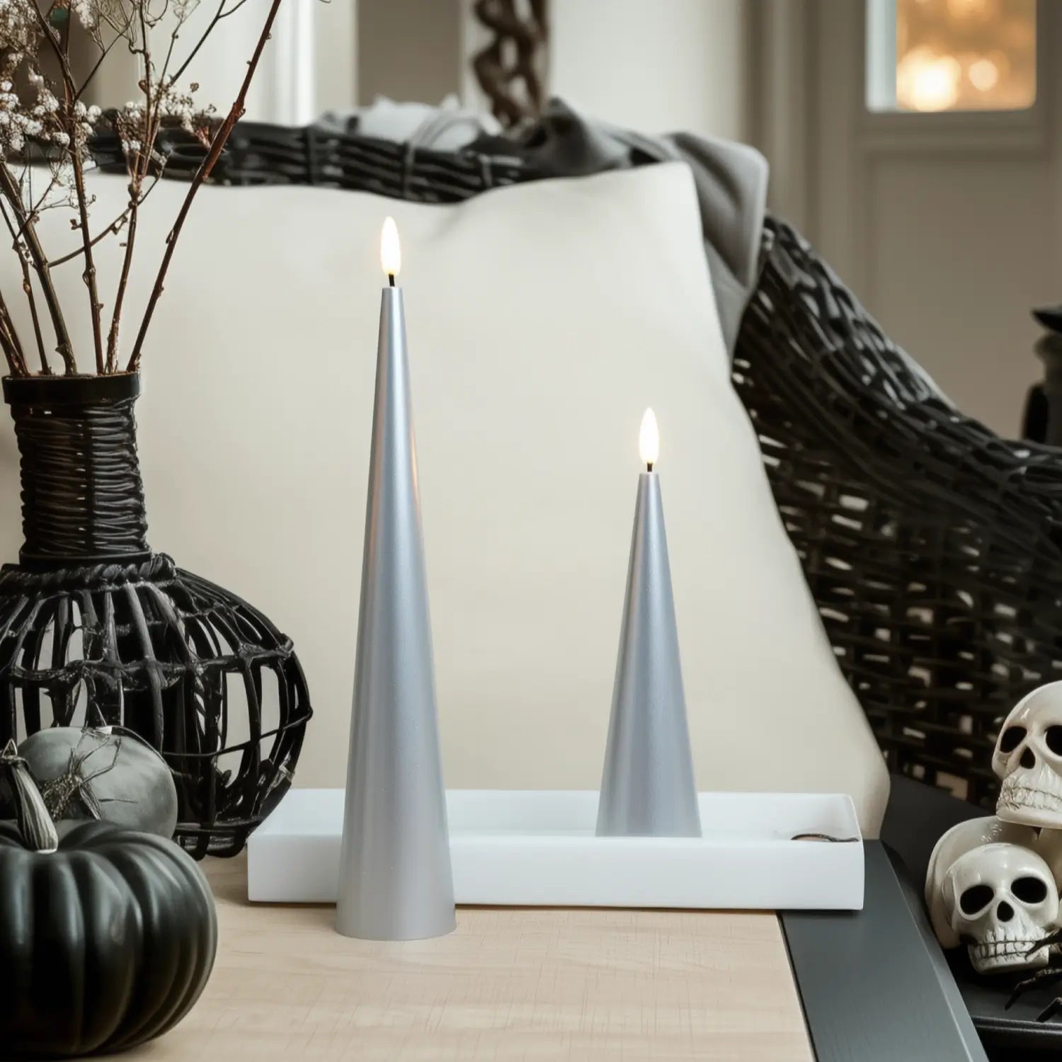 Two silver candles on a white base with decorative elements including pumpkins and skulls.