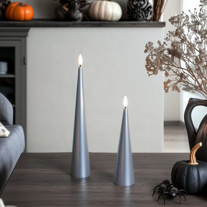 Two lit silver candles on a wooden surface with decorative elements in the background.