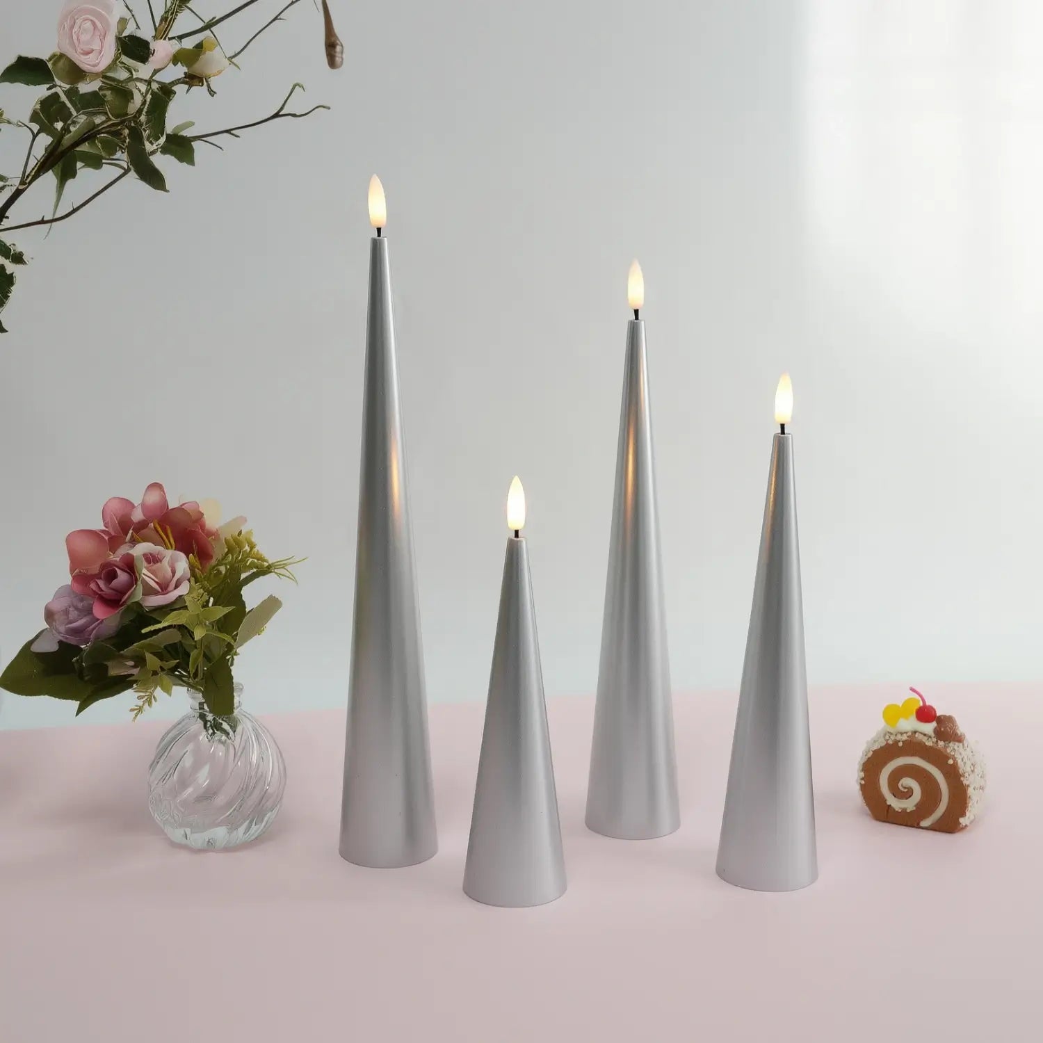 Set of four gray cone-shaped candles on a table with a fireplace and Christmas decorations in the background.