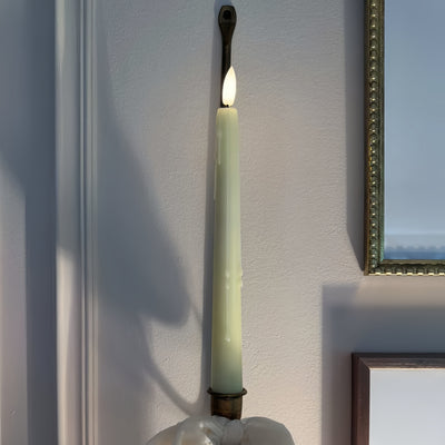 Tall green candle with a flame against a white wall.