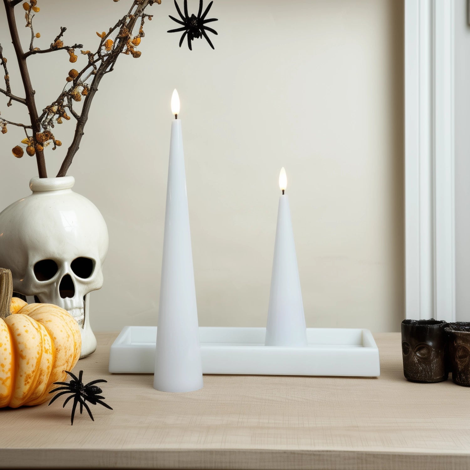 Halloween-themed decor with candles, skull, pumpkins, and spider webs on a neutral background.