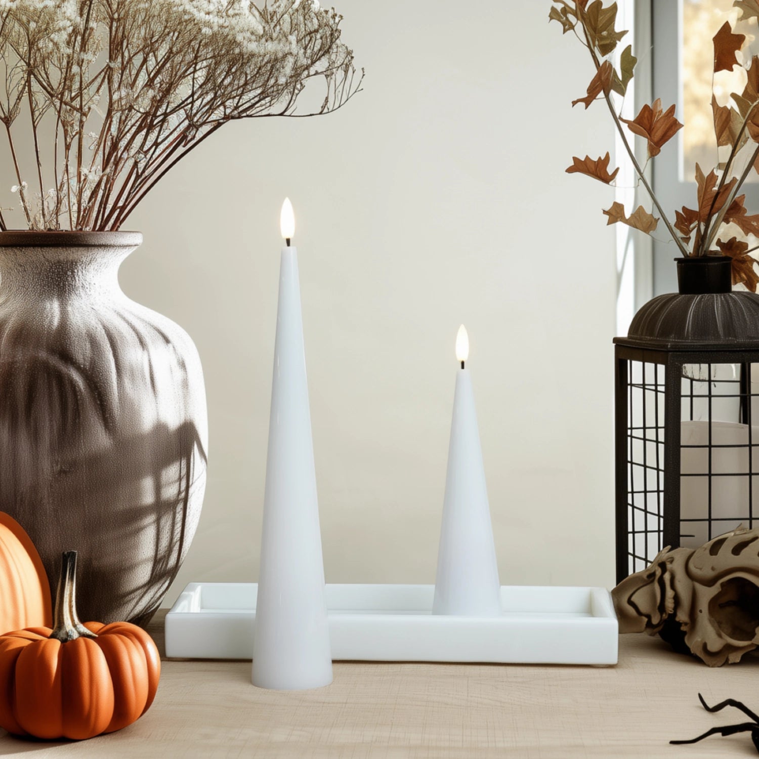 Decorative setup with candles, pumpkins, and dried plants on a neutral background