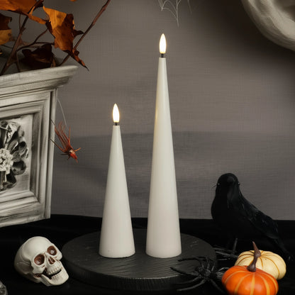 Two white cone-shaped candles on a dark surface with Halloween decorations.