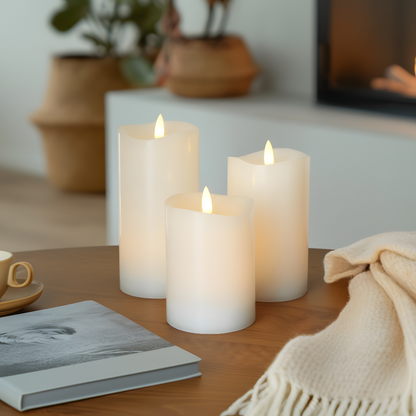 Three lit candles on a table with a book and a cup in a cozy indoor setting.