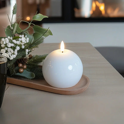 White spherical candle on a wooden tray with decorative elements on a table.
