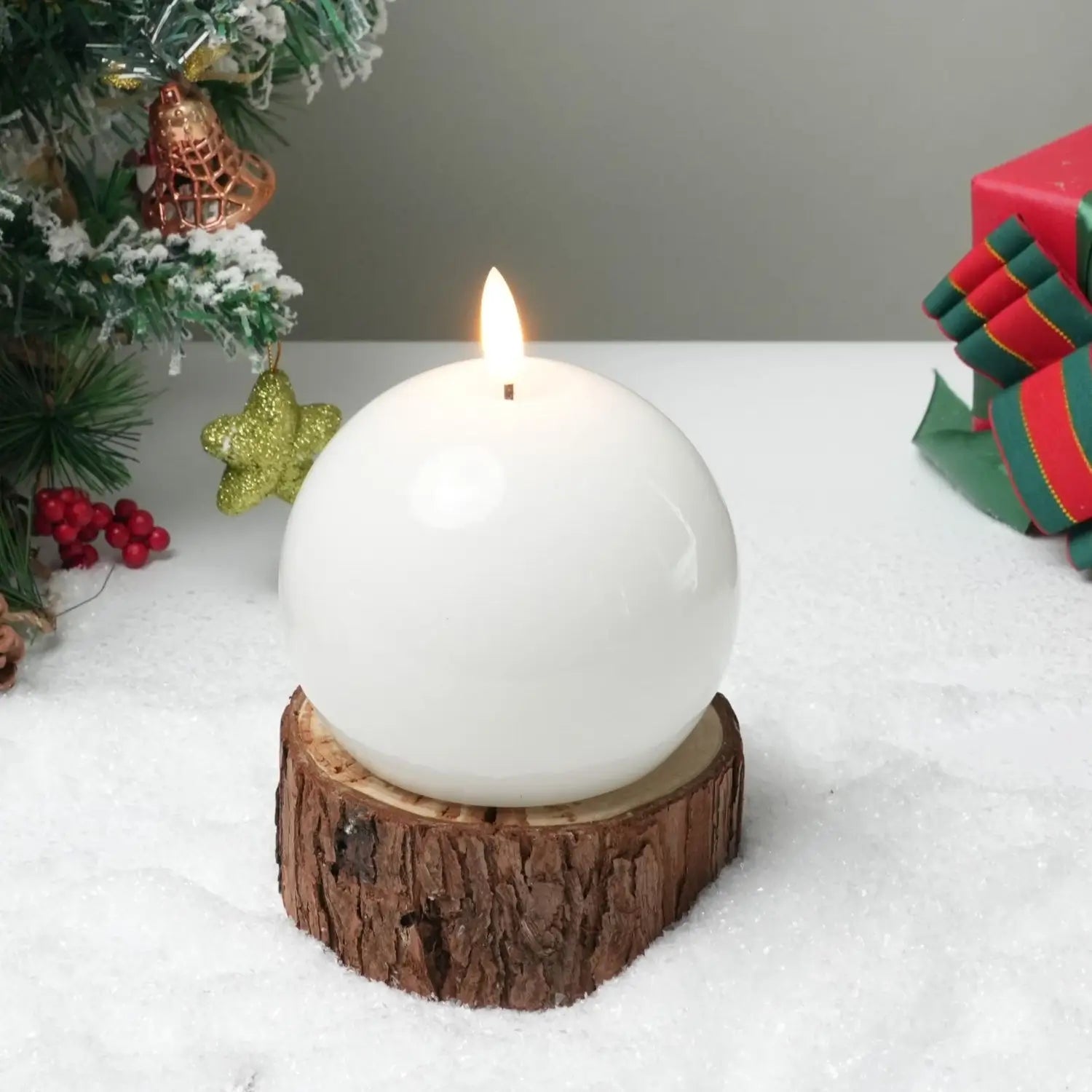 White spherical candle on a wooden base with Christmas decorations in the background