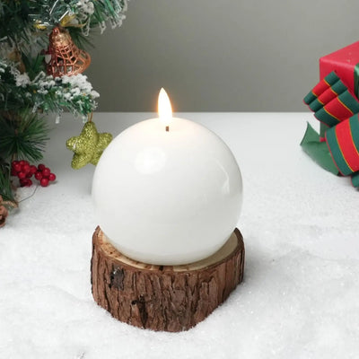White spherical candle on a wooden base with Christmas decorations in the background