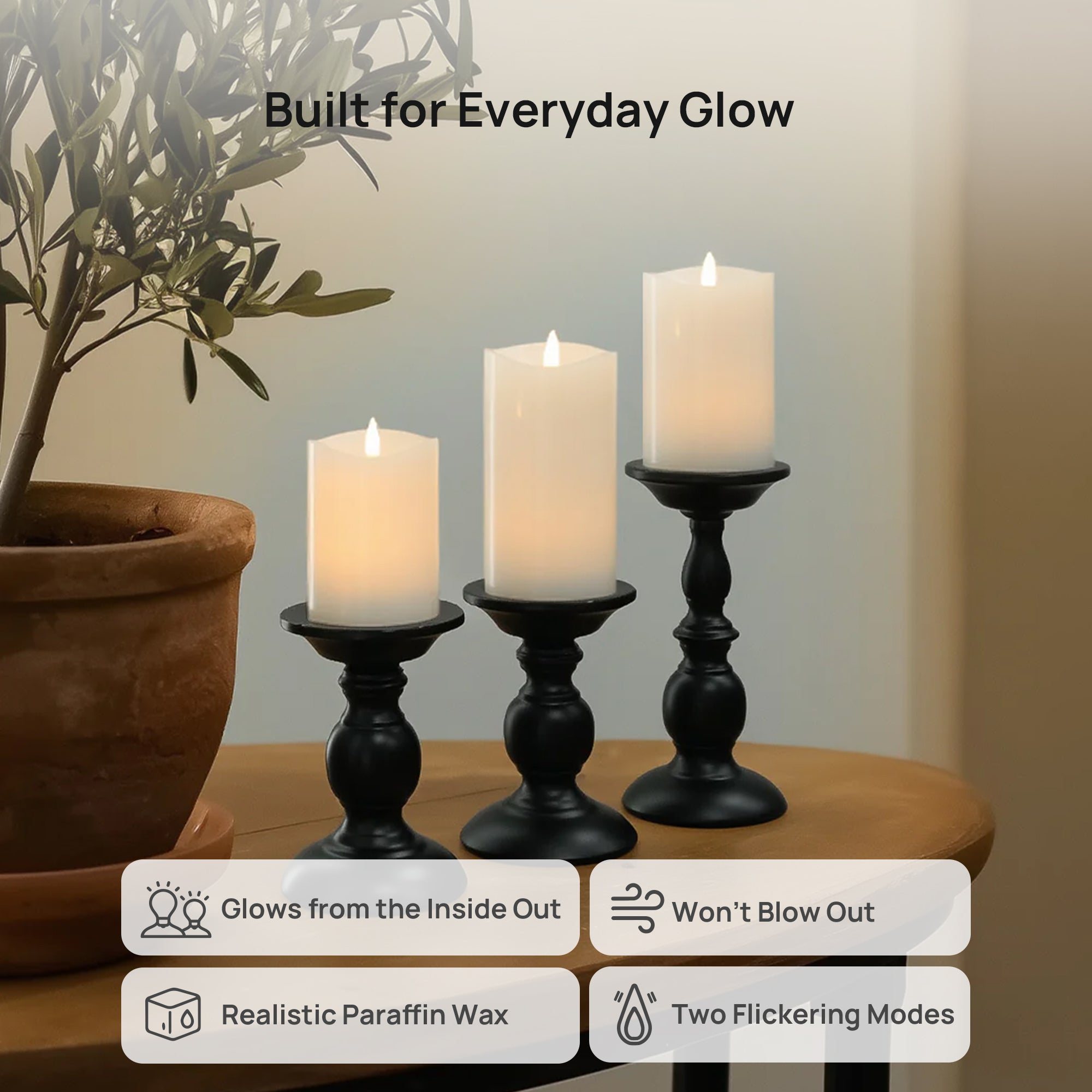 Three candles in black holders on a wooden table with a plant in the background.
