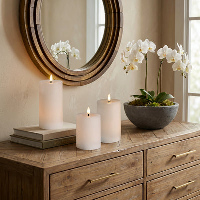 Wooden dresser with candles, a bowl of flowers, and a round mirror.